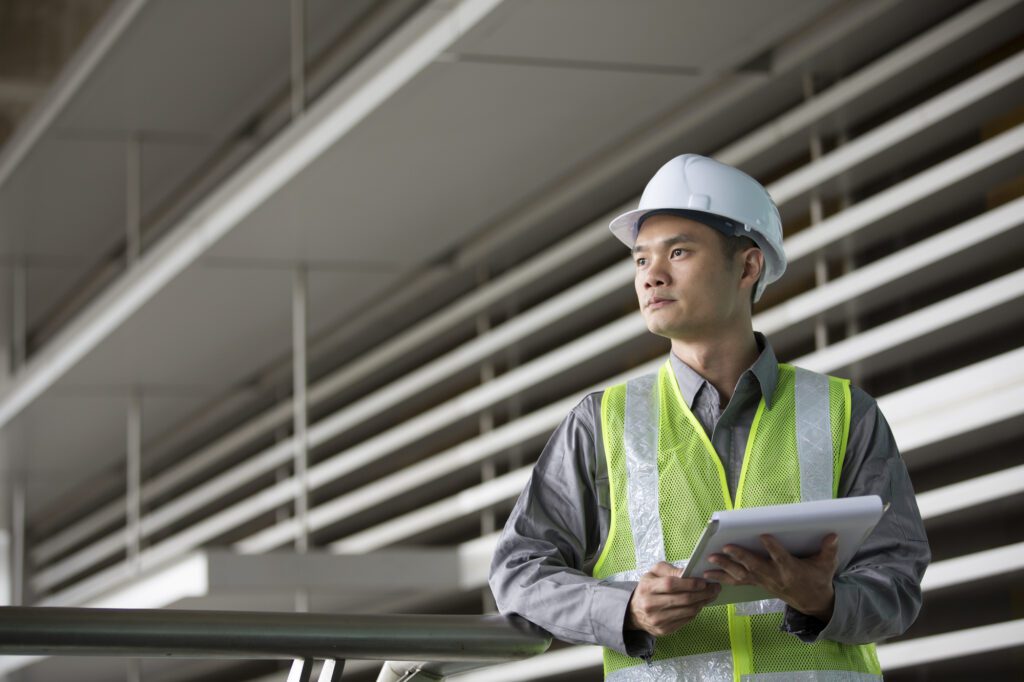 A man in safety vest holding papers and wearing a hard hat.