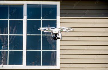 A white drone flying next to a window.