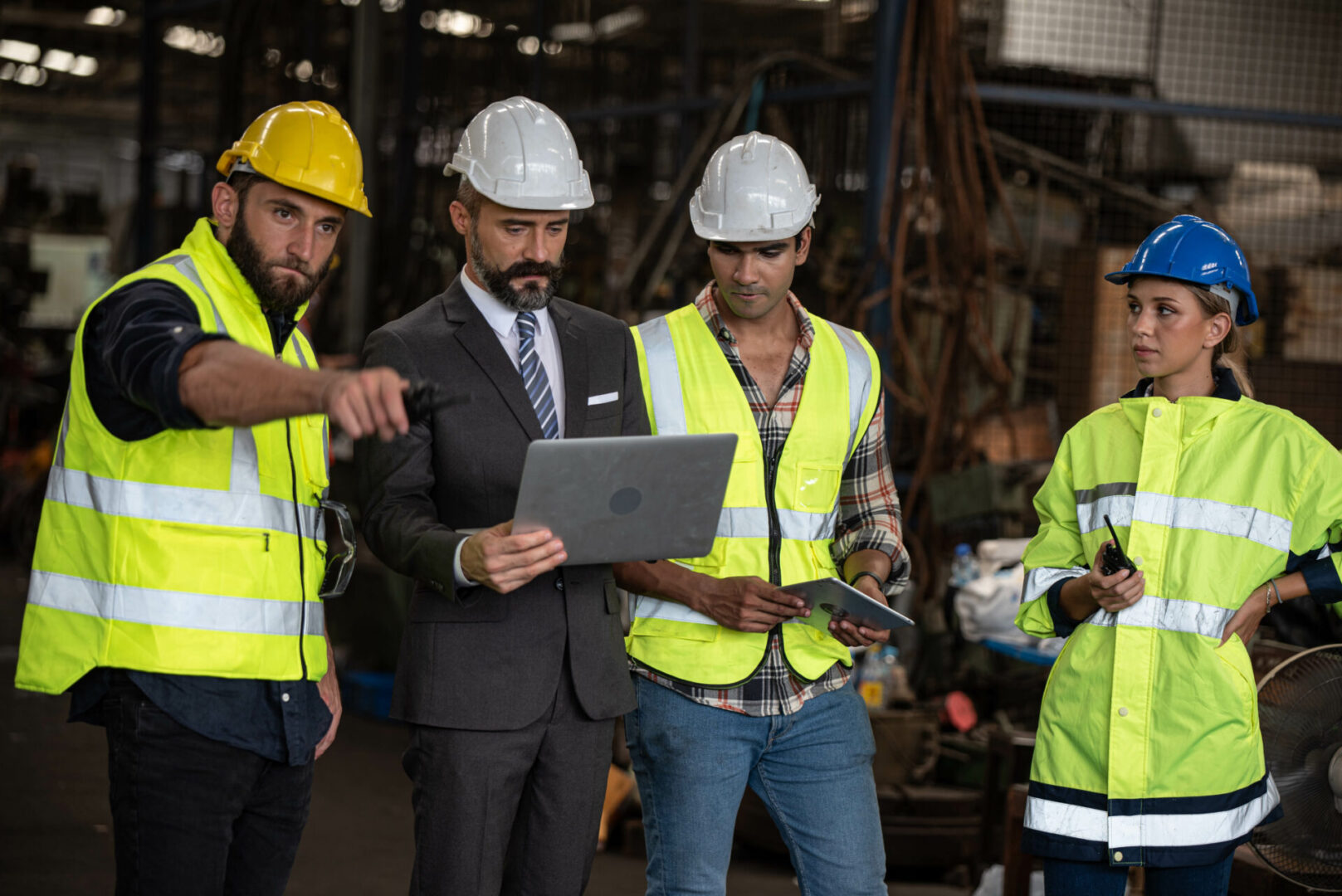 A group of men in hard hats and vests looking at something on a laptop.